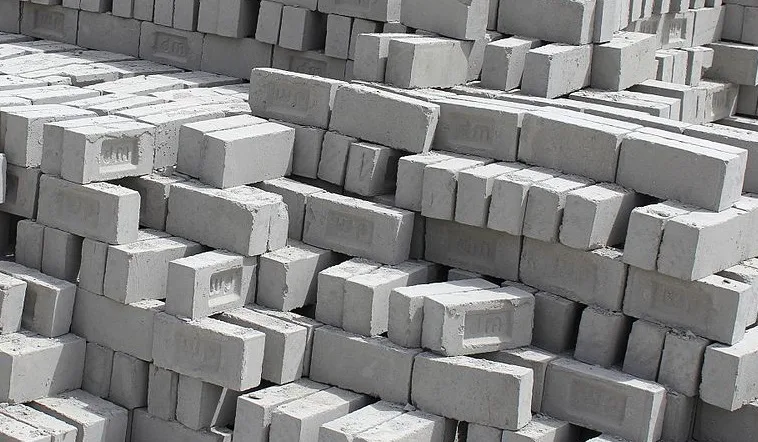 Stacks of grey fly ash bricks, each face stamped with an embossed maker's mark