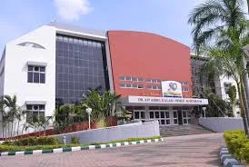 Modern institutional building with a curved red and glass facade behind a paved forecourt