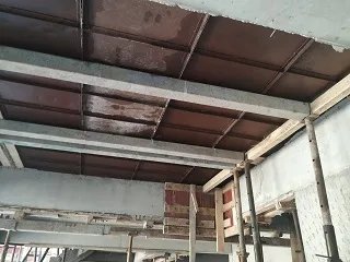 Underside of slab shuttering: brown panels between pale grey beams, supported on props inside a building under construction