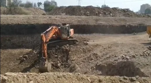 Orange tracked excavator digging at the foot of the excavated earth face, with spoil heaped along the top