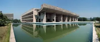 Concrete assembly building with a curved portico reflected in a long pool of water