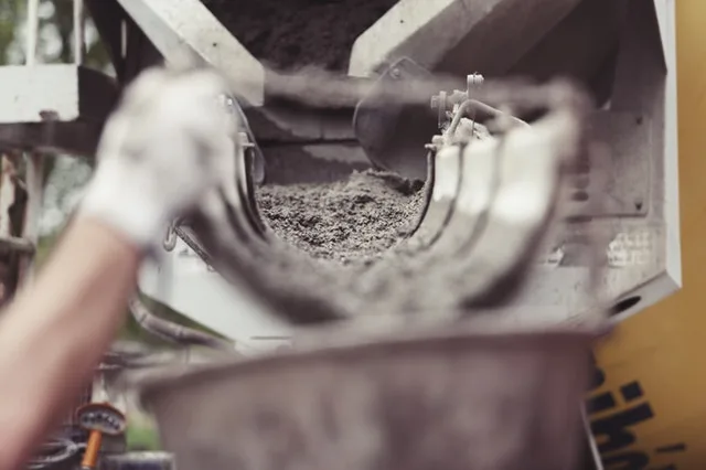 Concrete mixer truck chute discharging concrete into a bucket, with a gloved hand in the foreground