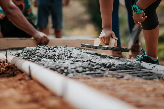 Worker levelling fresh concrete over rebar mesh with a wooden float inside a timber form