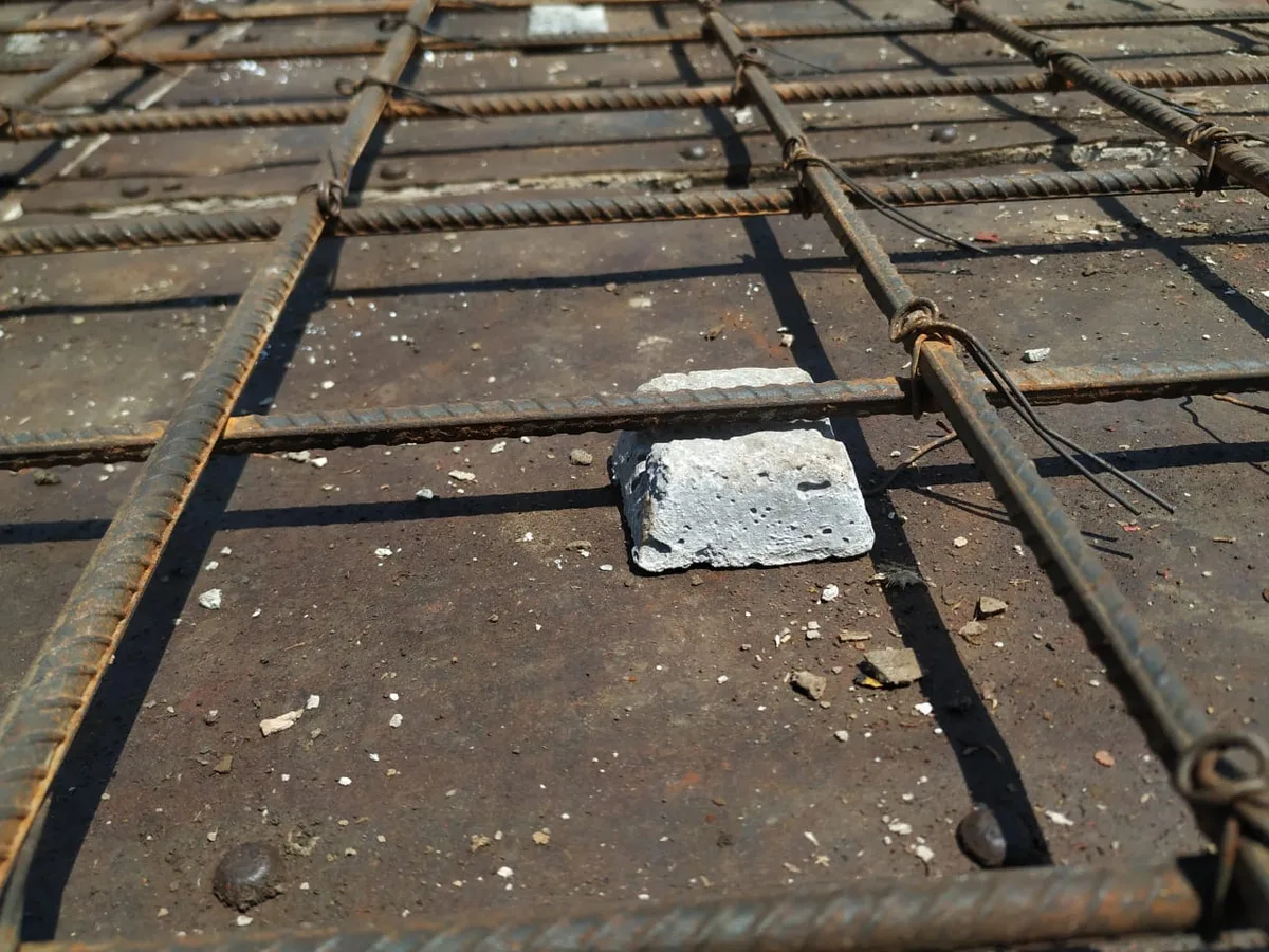 Square concrete cover block sitting under slab reinforcement on a steel shuttering plate