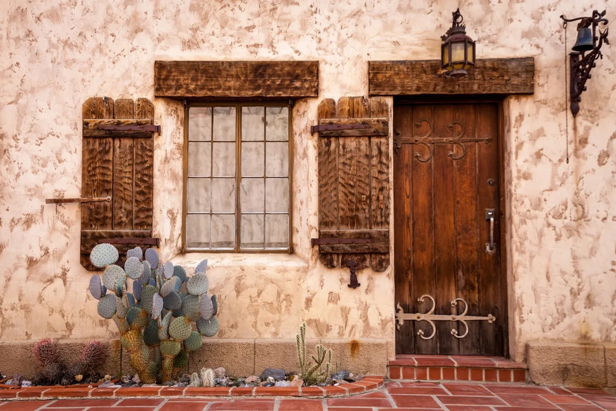Rustic plastered wall with heavy timber lintels above a shuttered window and a wooden door