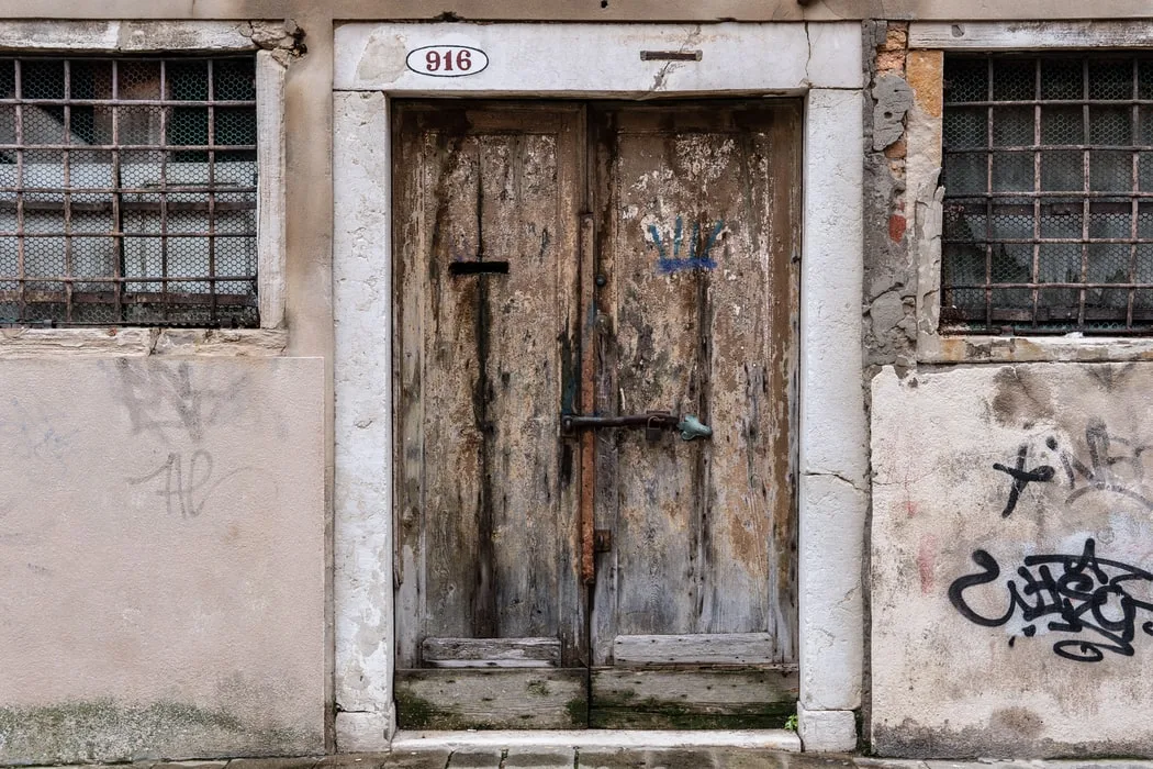 Weathered wooden double door in a stone surround with a stone lintel, barred windows on either side