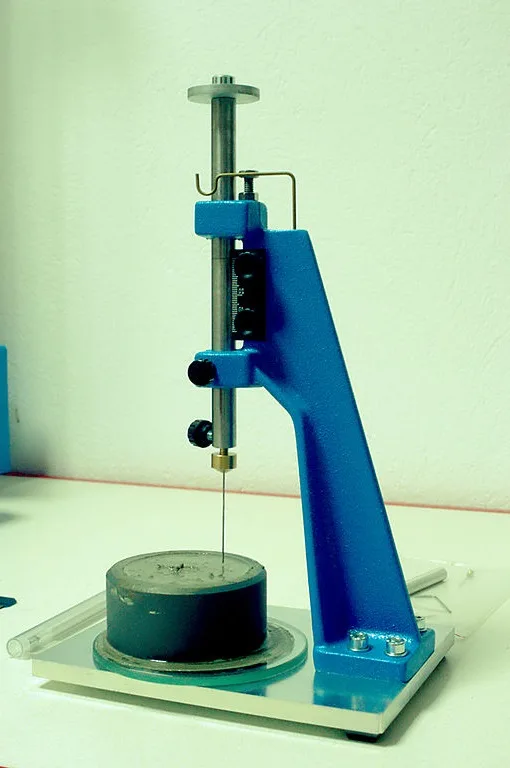 Blue Vicat apparatus with graduated scale and needle poised above cement paste in a mould on a glass plate