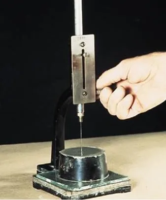 Vicat apparatus with a hand lowering the needle onto cement paste in the mould