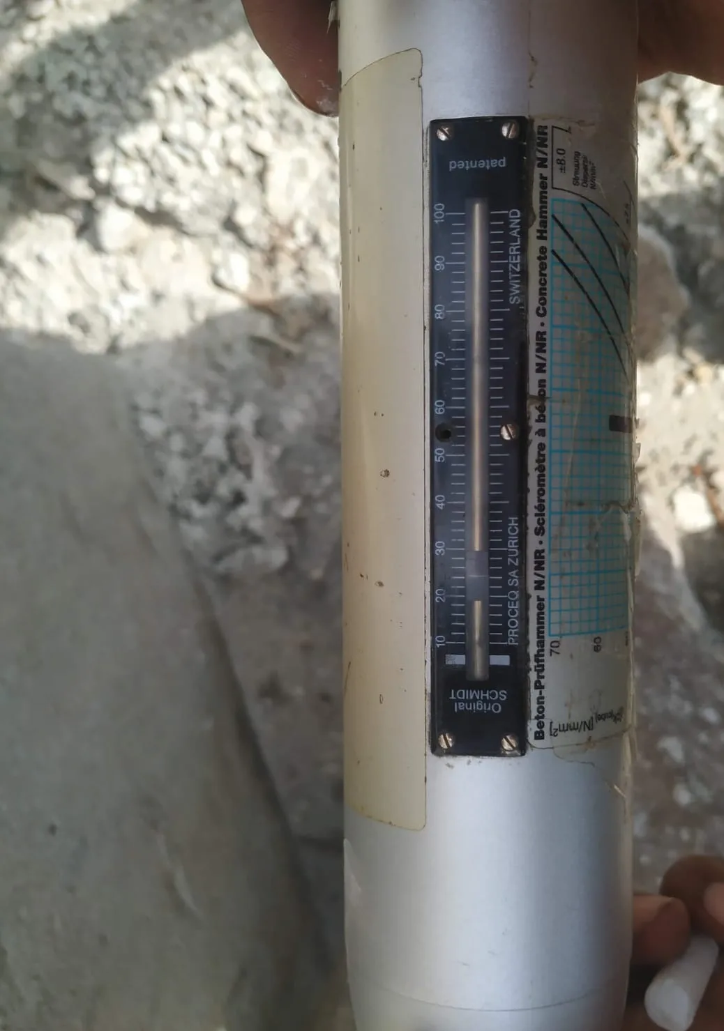 Close-up of an Original Schmidt rebound hammer's 10 to 100 rebound scale and calibration chart, held on site
