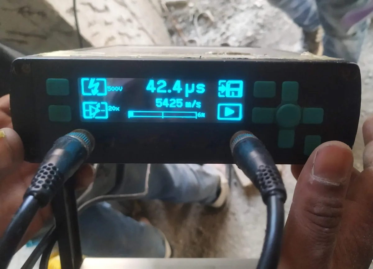 Ultrasonic pulse velocity meter held on site, display reading 42.4 µs transit time and 5425 m/s