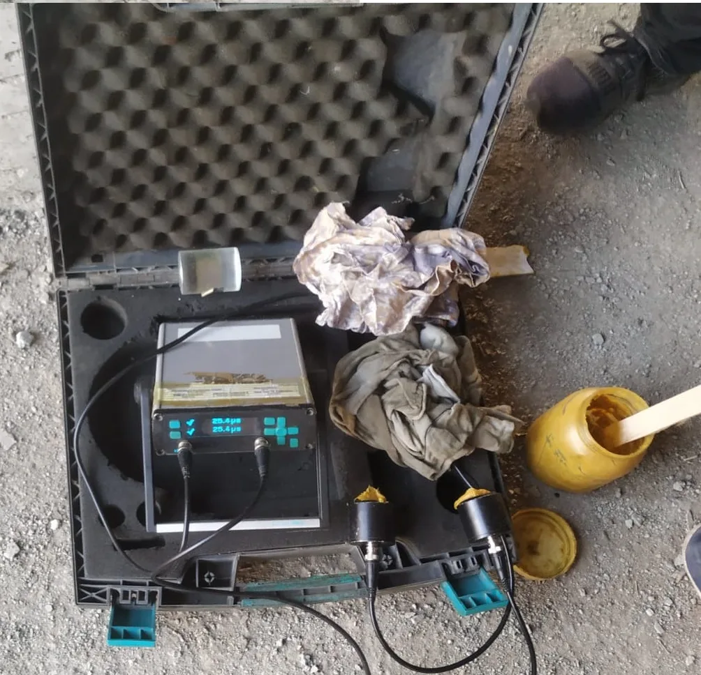 UPV meter in its foam-lined carry case on the ground with two transducers, cables, rags and an open jar of yellow paste