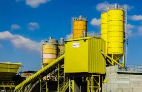 Concrete batching plant with tall yellow cement silos and a conveyor against a blue sky