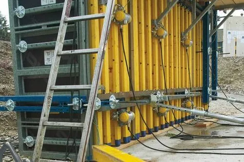 External vibrators clamped to the outside of yellow wall formwork panels, with a ladder and power cables