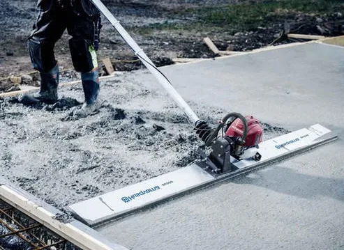 Worker in boots guiding a petrol-engined vibrating beam screed across a freshly poured concrete slab
